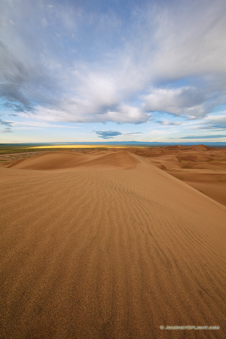 Dunes flow into the west at Great Sand Dunes National Park as white clouds lazily float above. - Great Sand Dunes NP Picture