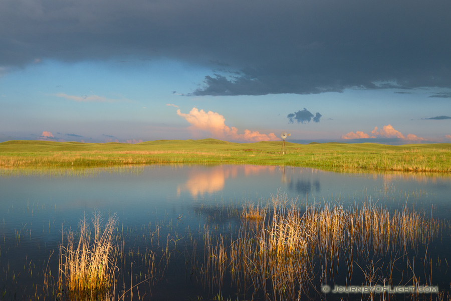 A windmill and storm clouds are reflected in a small lake in the Sandhills of Nebraska. - Nebraska Photography