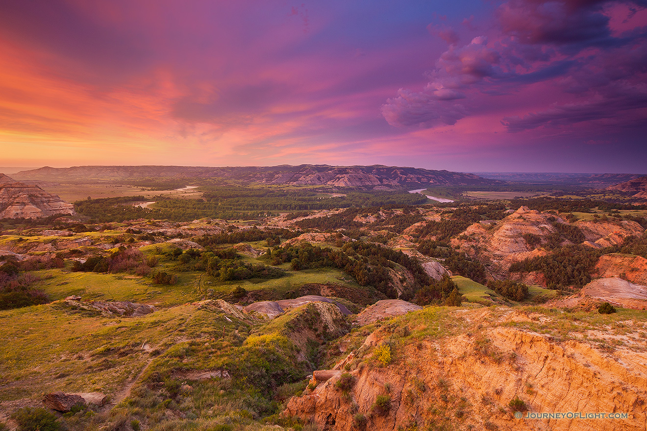Above a bend in the Little Missouri River in the North Unit of Theodore Roosevelt National Park, clouds glow purple and orange as the sun just begins to rise above the horizon. - North Dakota Picture