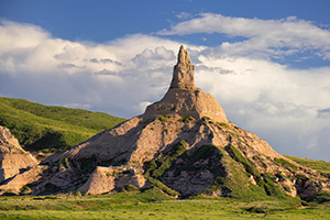 Clouds gather behind Chimney Rock as the glow of the late afternoon sun illuminates its western side. - Nebraska Photograph