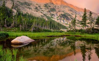 Deep in the backcountry of Rocky Mountain National Park, a small tarn close to Thunder Lake reflects the beautiful mountains as they glow with the light of the rising sun..