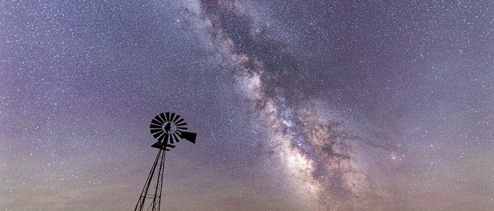 The Milky Way arcs behind a lone windmill in the Sandhills of Nebraska.